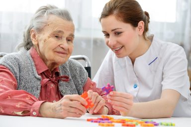 Elder care nurse playing jigsaw puzzle with senior woman in nursing home