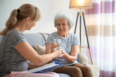 Caregiver giving glass of water to senior woman at home